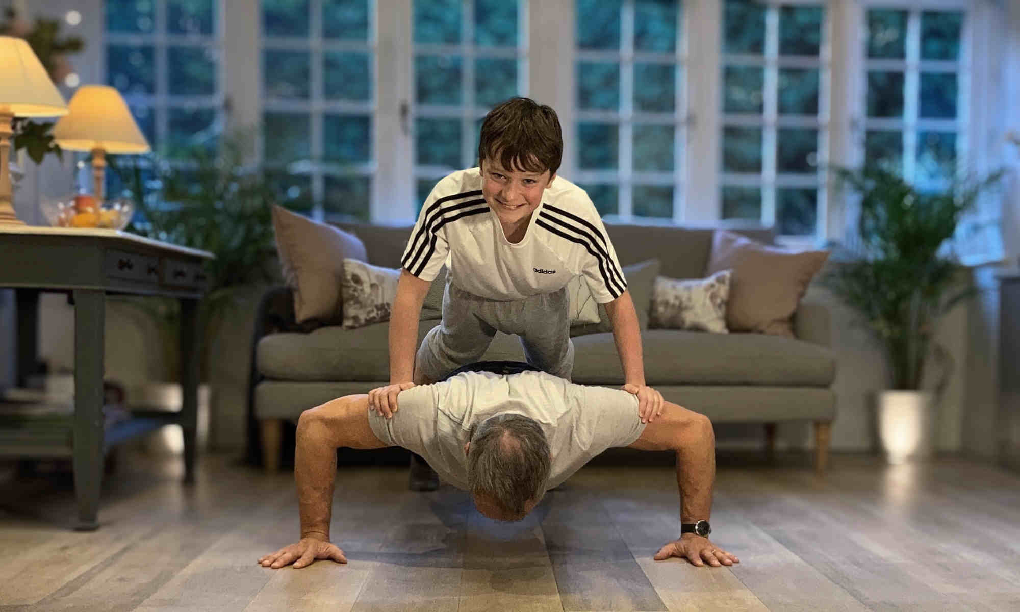 son doing a press up on back of father who is also doing a press up.