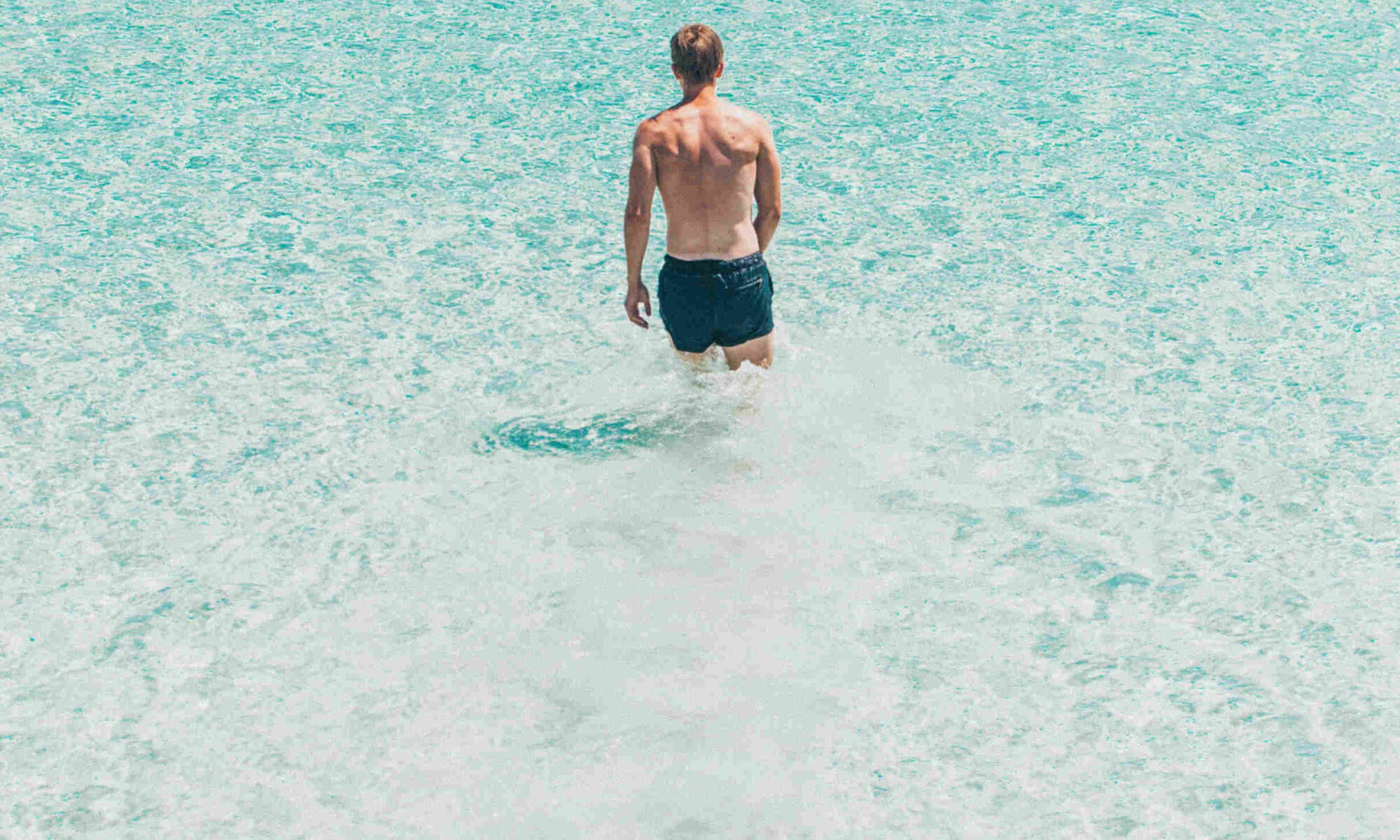 Healthy man wading into clear blue sea